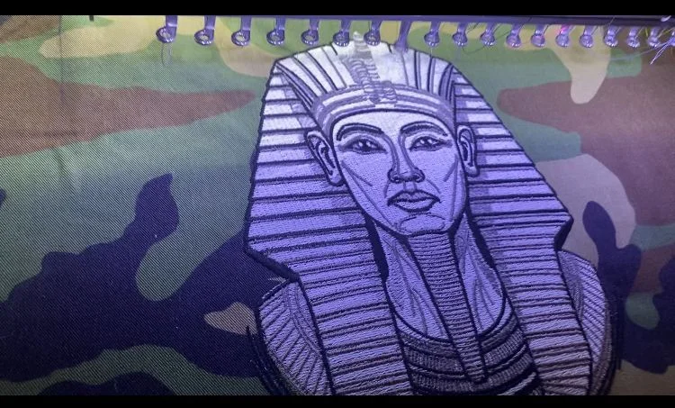Photo from GMB's existing apparel gallery; shown for decoration and product planning, not current stock availability. This finished garment does not establish which printing method was used. Multicolor garment graphic on camouflage fabric, illustrating printed artwork detail
